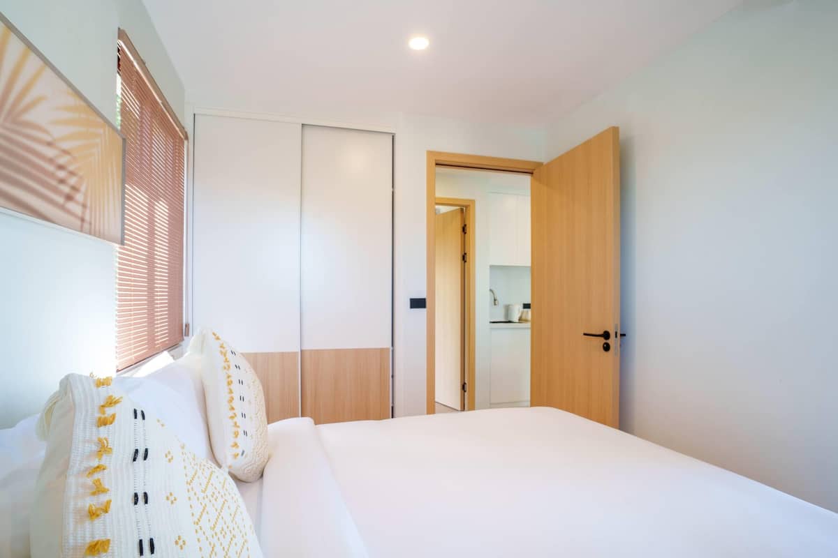 Una habitación de hotel moderna con una cama grande, un armario y un baño visible a través de una puerta abierta.