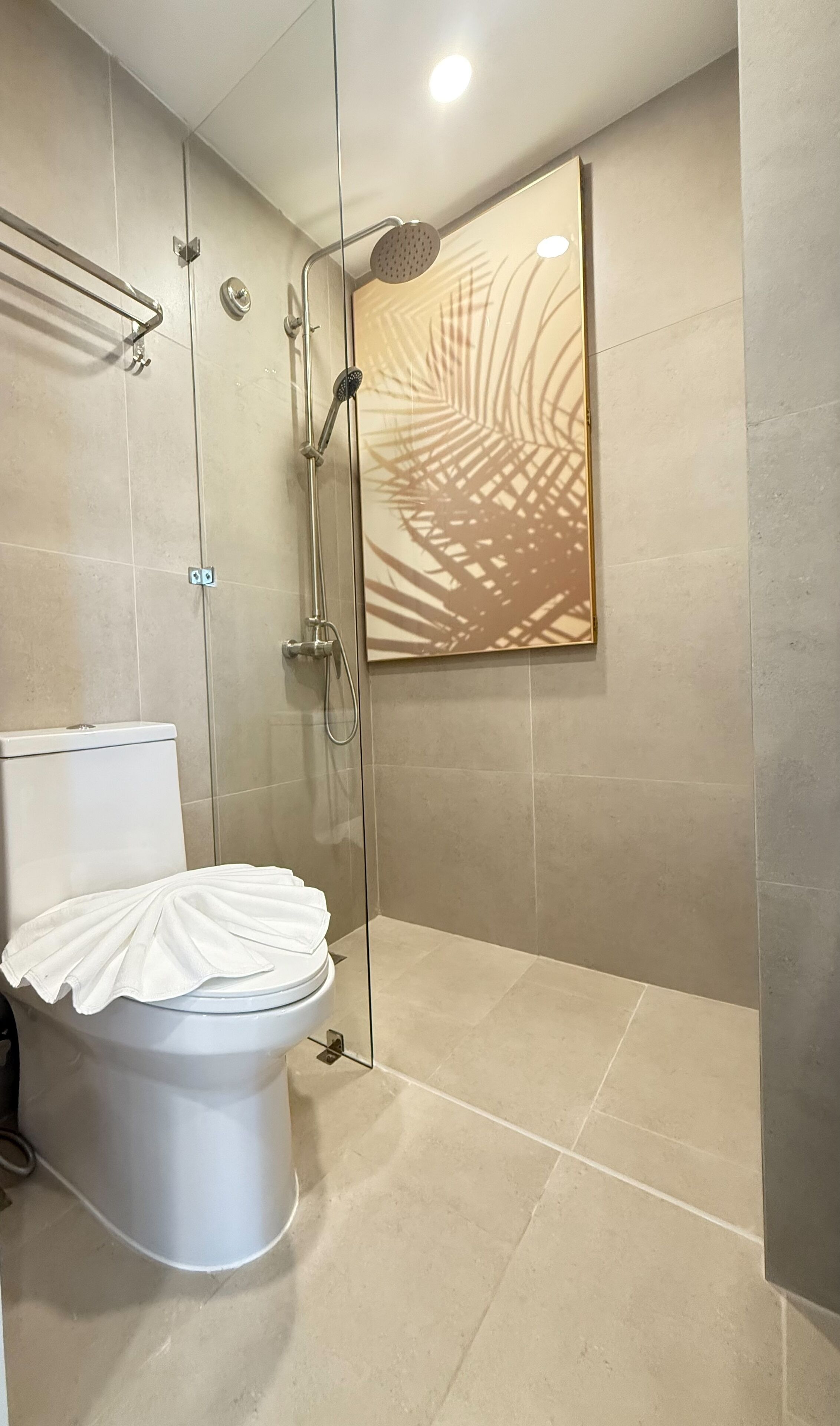 A modern bathroom with a glass-enclosed shower, a toilet with a white lid, and a large mirror with a palm leaf design.