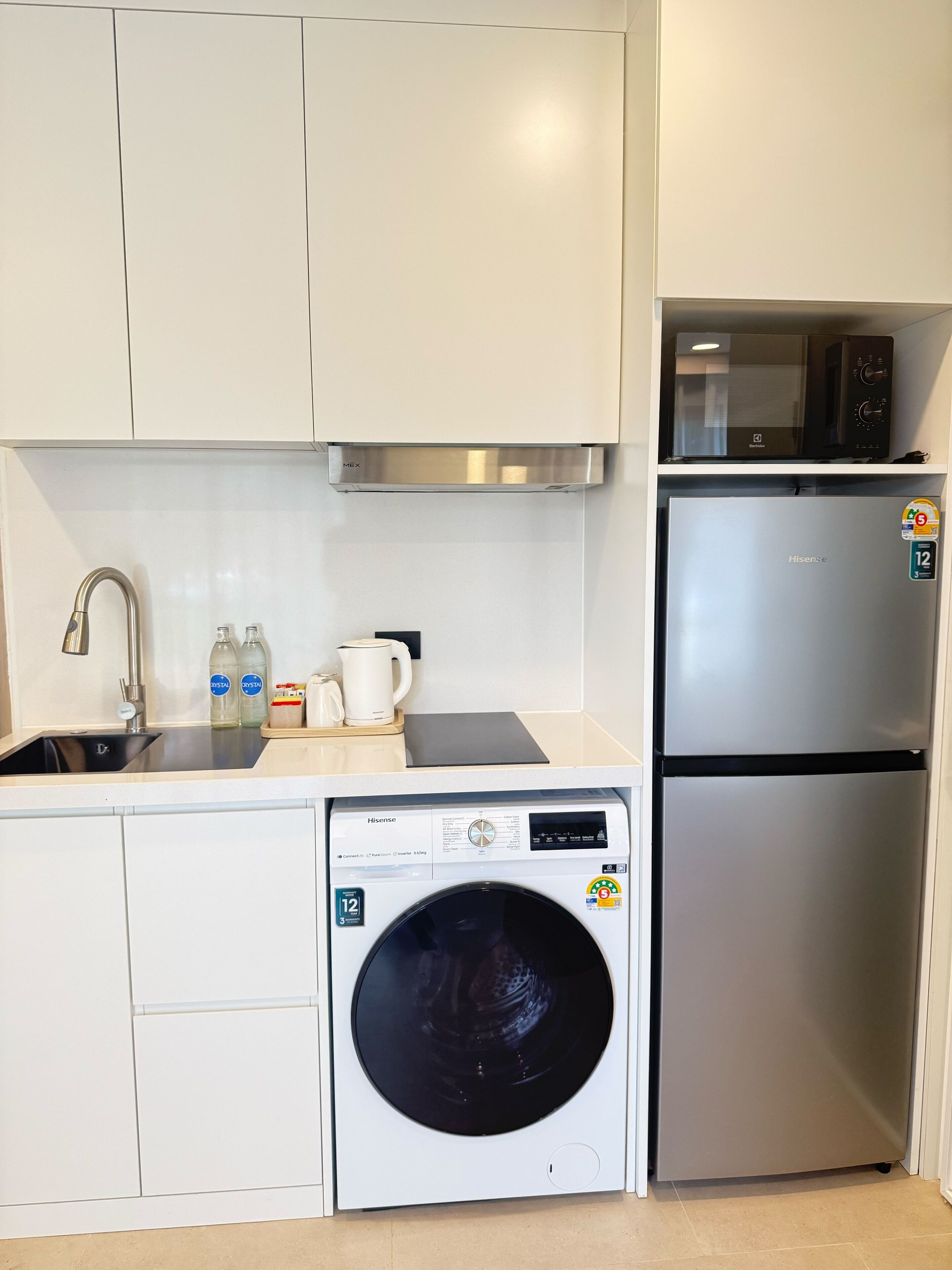 Une cuisine compacte équipée d’un réfrigérateur en acier inoxydable, d’un lave-linge, d’un four à micro-ondes et d’un évier avec un robinet.