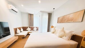 A modern hotel room with a large bed, a seating area with cushions, a flat-screen TV, and a ceiling-mounted air conditioner. - Wyndham Garden Samui Wing (Koh Samui)