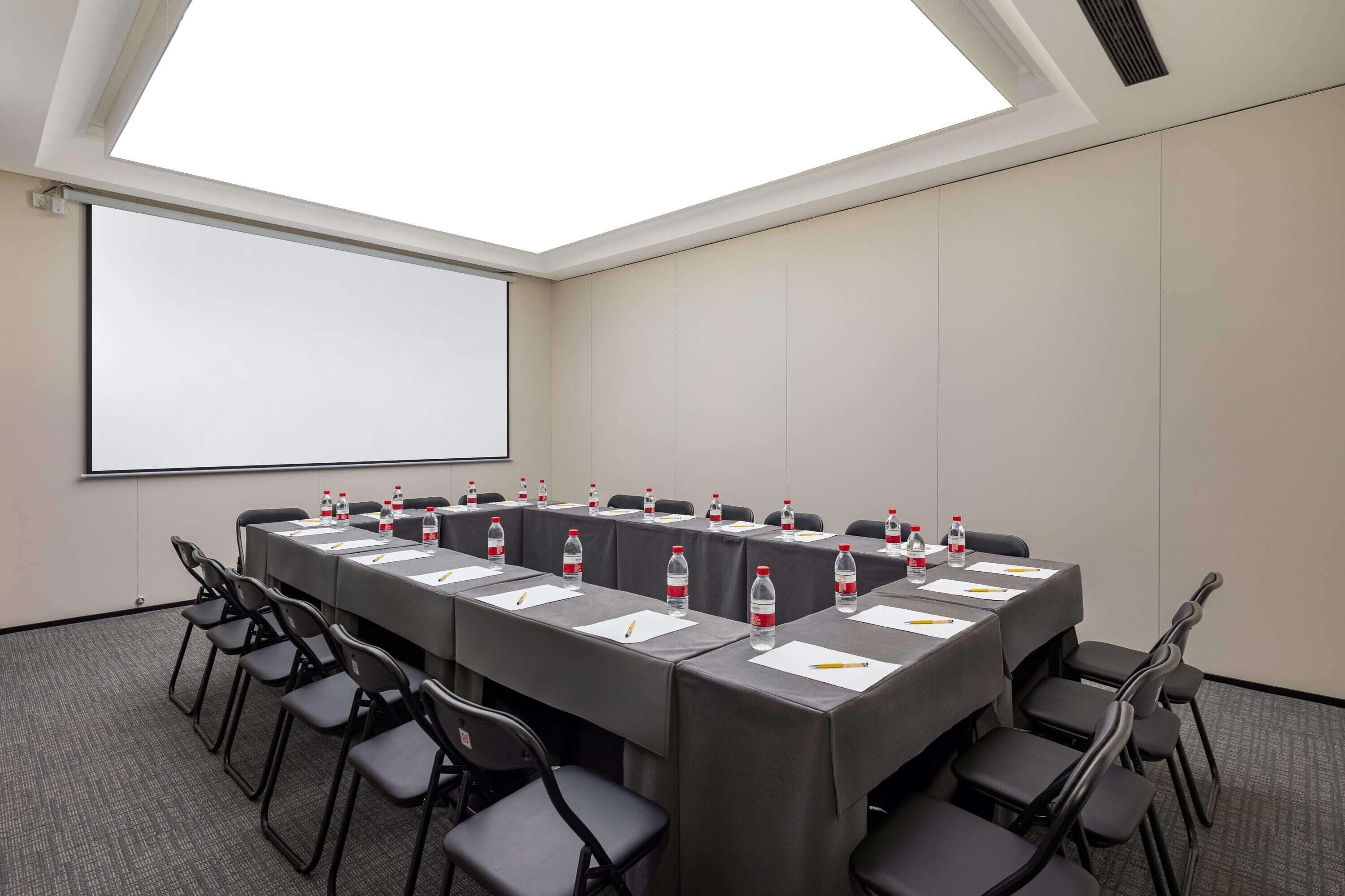 A conference room with a long table, chairs, water bottles, and a projector screen.