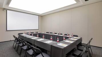 A conference room with a long table, chairs, water bottles, and a projector screen.