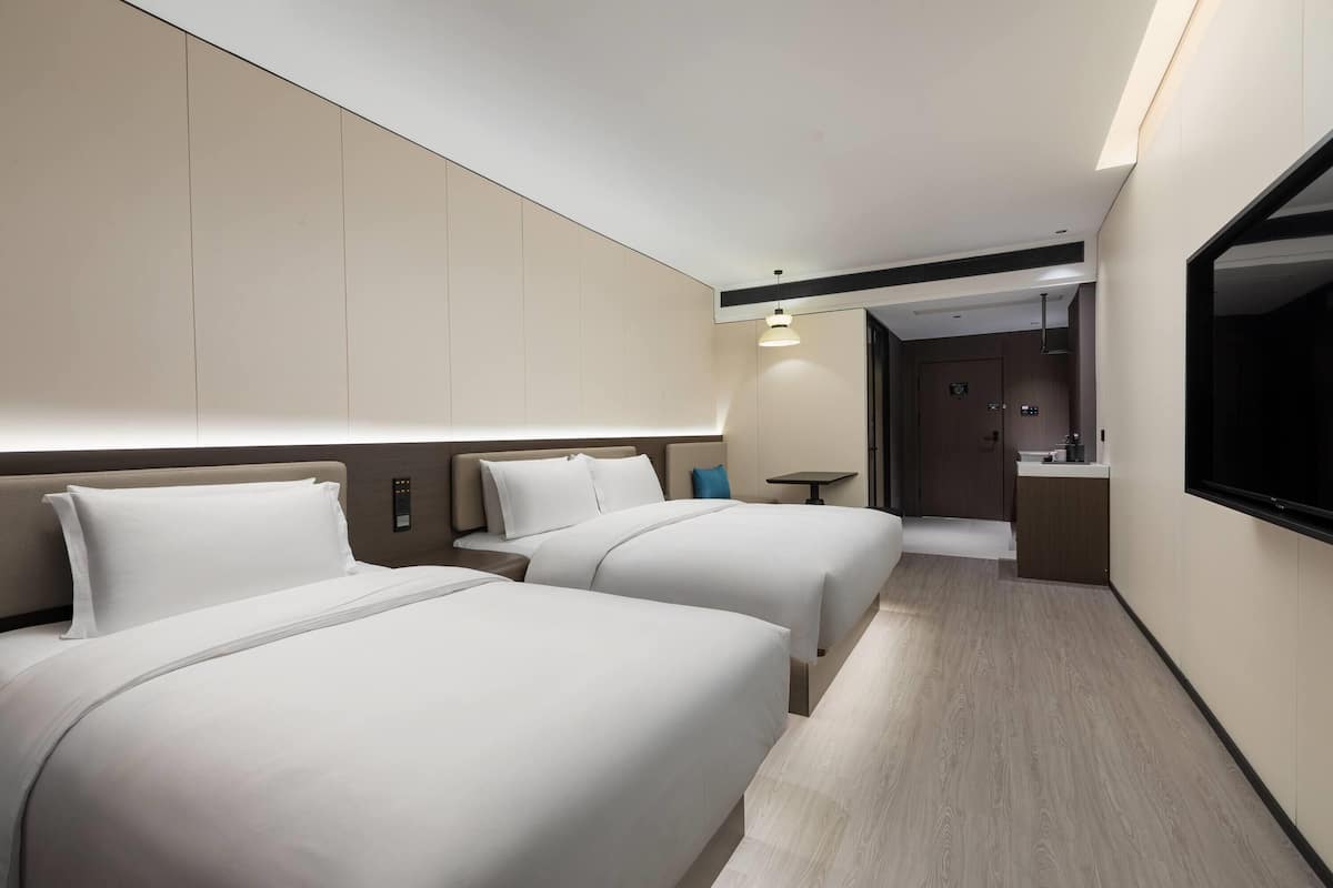 Een hotelkamer met twee bedden, een televisie, een tafeltje en een badkamer die door een open deur zichtbaar is.