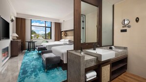 Habitación de hotel con una cama grande, una zona de estar con mesa y sillas, un baño con espejo amplio y lavamanos, y vistas al exterior.