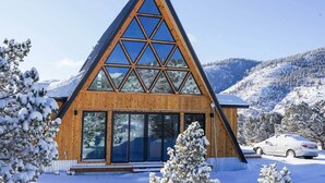 A wooden cabin with a triangular roof and large windows, surrounded by snow-covered trees and mountains. - Hello Dreamer A-Frame (Maysville)