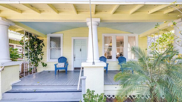 A porch with a white column, blue chairs, and a door.