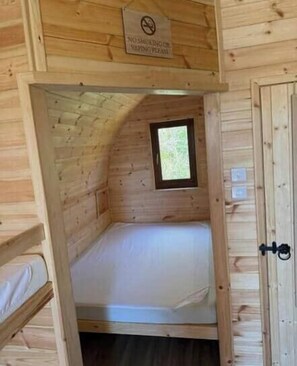 Une petite cabane en bois avec un lit simple, une fenêtre et une porte.