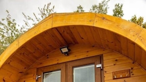 A wooden cabin with a curved roof, a double door with glass panels, and a small porch area. - Livi Family Pod - hot tub (Thirsk)