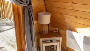 Tunnelmallinen huone, jossa on puinen katto, seinälle asennettu televisio, pieni pöytä lampun kanssa ja ikkuna, jossa on verhot.