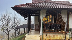 Un espace extérieur abrité, doté d’une terrasse, auquel on accède par un escalier en pierre, et entouré d’arbres sans feuilles et d’un vignoble en arrière-plan.