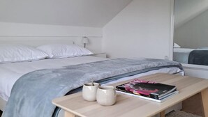 Une chambre à coucher avec un lit, une table de chevet sur laquelle se trouvent des livres et des tasses, et une fenêtre.
