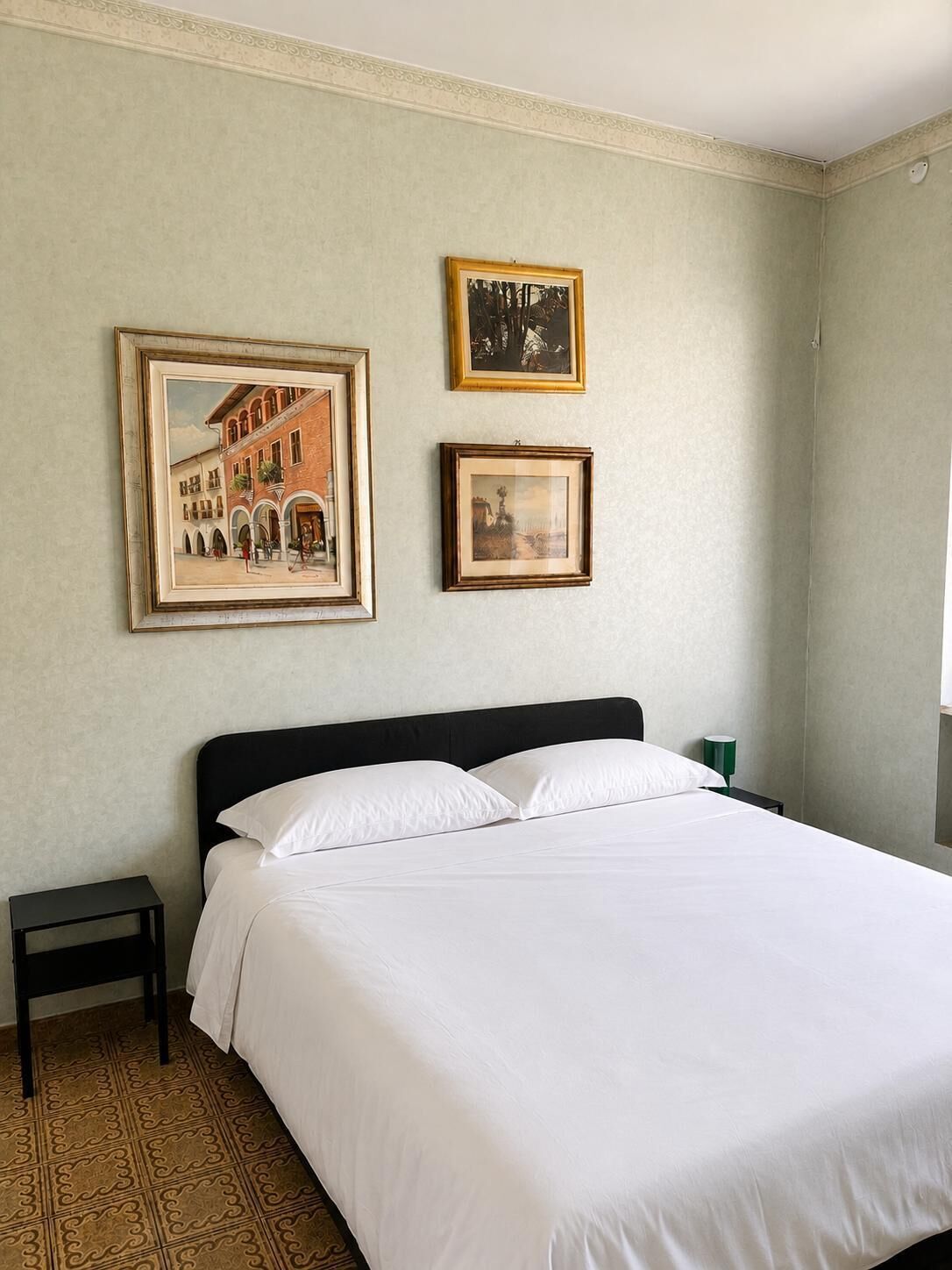 Une chambre à coucher avec un lit, une table de chevet et deux tableaux encadrés accrochés au mur.