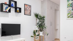 Ein modernes Wohnzimmer mit Flachbildfernseher, Bücherregal, Topfpflanze und Kleiderschrank.