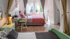 Un dormitorio acogedor con cama, escritorio y silla. Hay cortinas, una lámpara y una ventana con vistas a edificios.