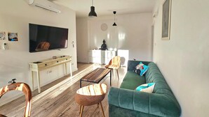 Una sala de estar con un televisor de pantalla plana, un sofá verde, una mesa de centro de madera y un aparador blanco.