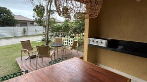 Un pati exterior amb taula i cadires de fusta, una barbacoa i una tanca blanca al fons.