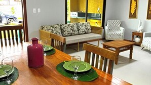 A dining area with a wooden table set for four, a sofa, and a patterned armchair. - Yellow House - Pitinga Beach - Arraial d'Ajuda (Arraial d'Ajuda)