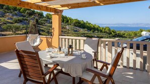 A covered outdoor seating area with a table set for two, overlooking a scenic landscape with trees and a view of the sea. - Beautiful home in Supetar with WiFi (Supetar)