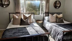 Quarto com duas camas, um ventilador de teto e uma janela com cortinas.