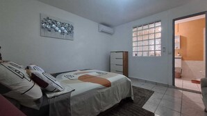 Un dormitori amb un llit, una petita taula de nit, una finestra i una porta que dona a un bany.