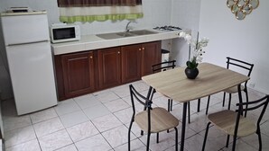 Cuina compacta amb nevera, microones, rentapelats i fogó. Hi ha una taula de dinar amb caires i una orquídia en test.