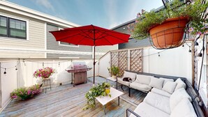 A patio with a red umbrella, outdoor furniture, a grill, and hanging planters. - Stylish East Boston Gem, Near Downtown, T and Airport (Boston)
