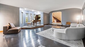 Uma sala de estar ampla com um piano, uma escada e um sofá moderno.