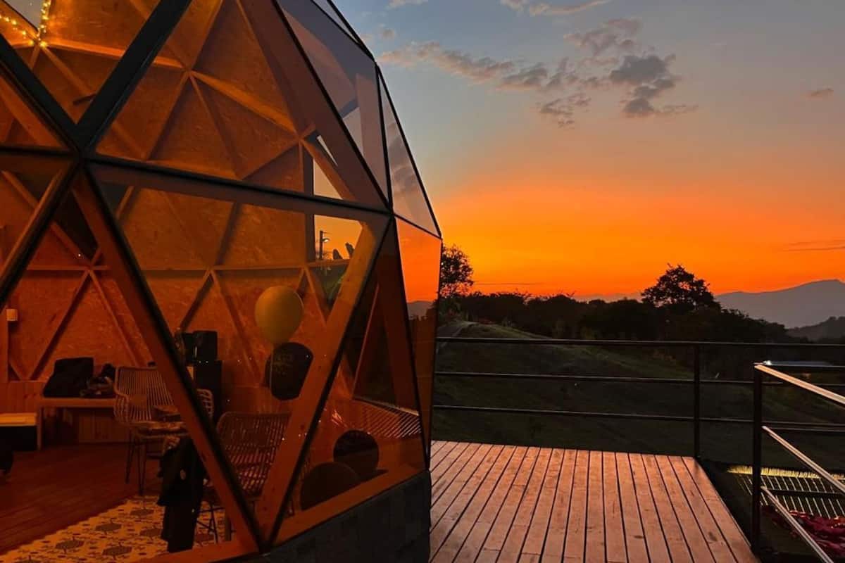 A geodesic dome structure with a wooden deck and seating area, overlooking a landscape at sunset.