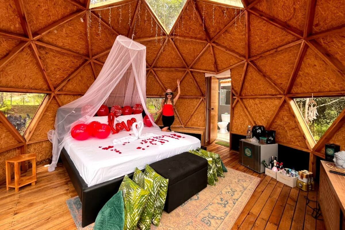 A cozy, octagonal wooden room with a bed, a small table, and a bench.