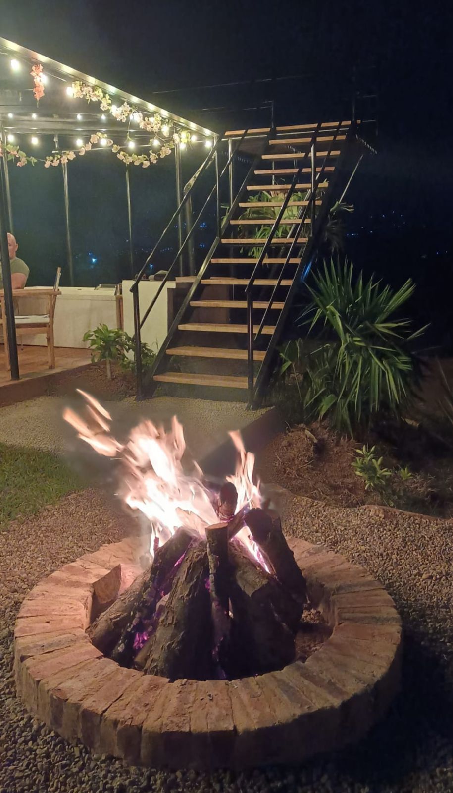 Ein runder Feuerkorb aus Stein, umgeben von Kies, mit einer Treppe und einem Geländer im Hintergrund.