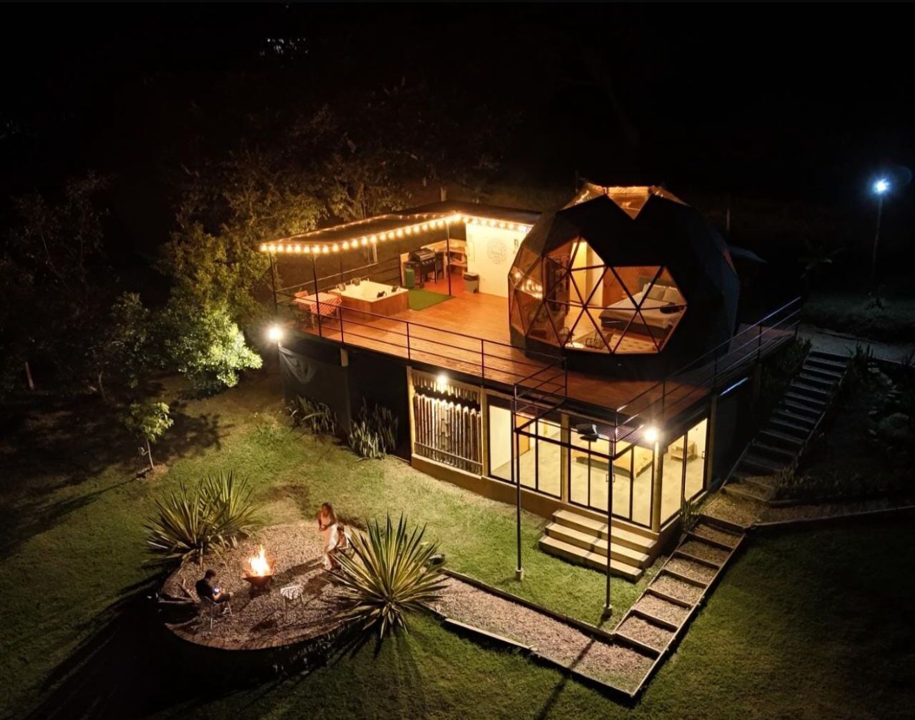 Une maison moderne dotée d’une grande structure en forme de dôme, d’un patio couvert et d’un espace aménagé avec un foyer.