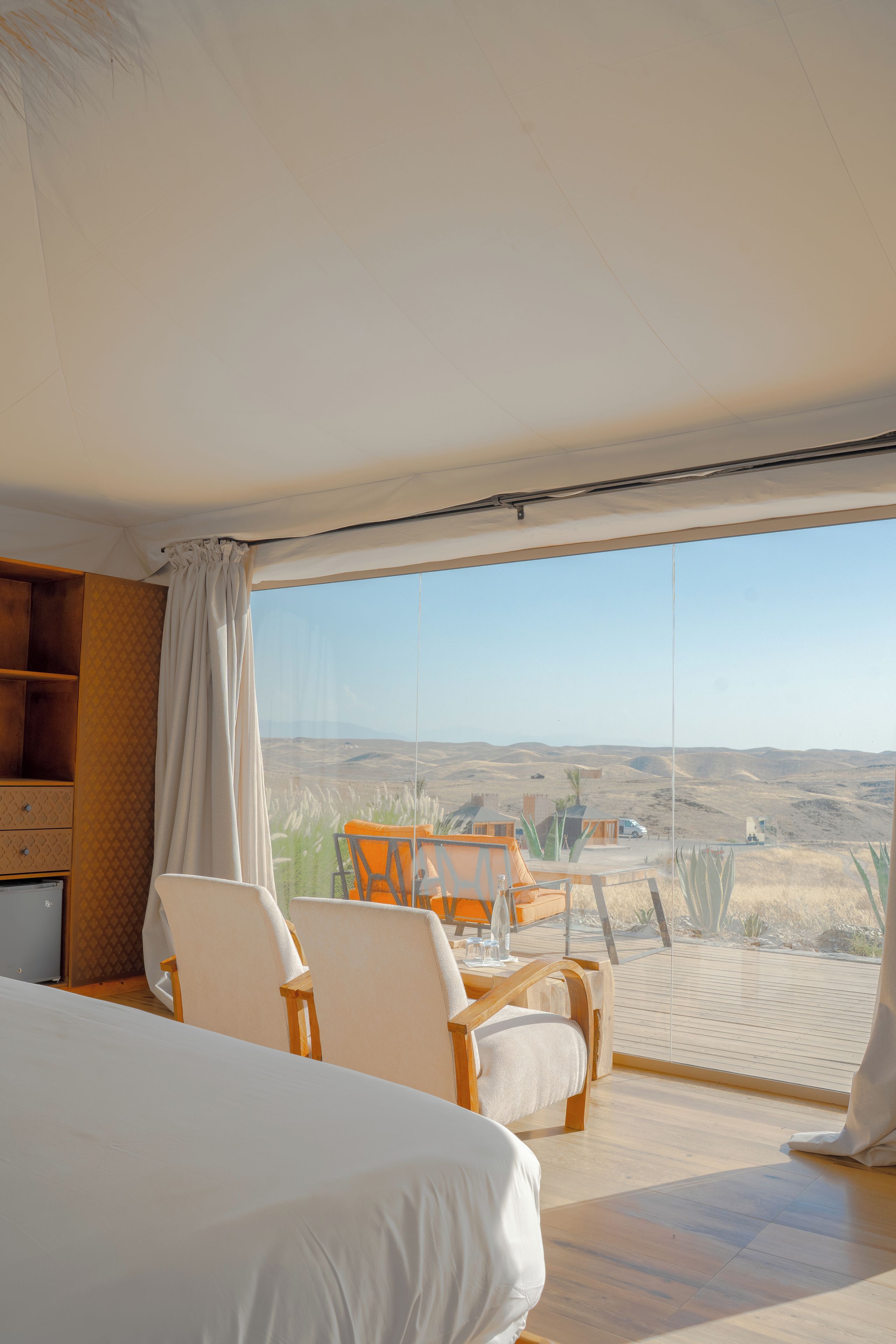 A room with a large bed, a dining table with chairs, and a view of a desert landscape.