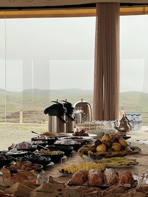 A buffet table with various food items and a view of a mountainous landscape through a window.