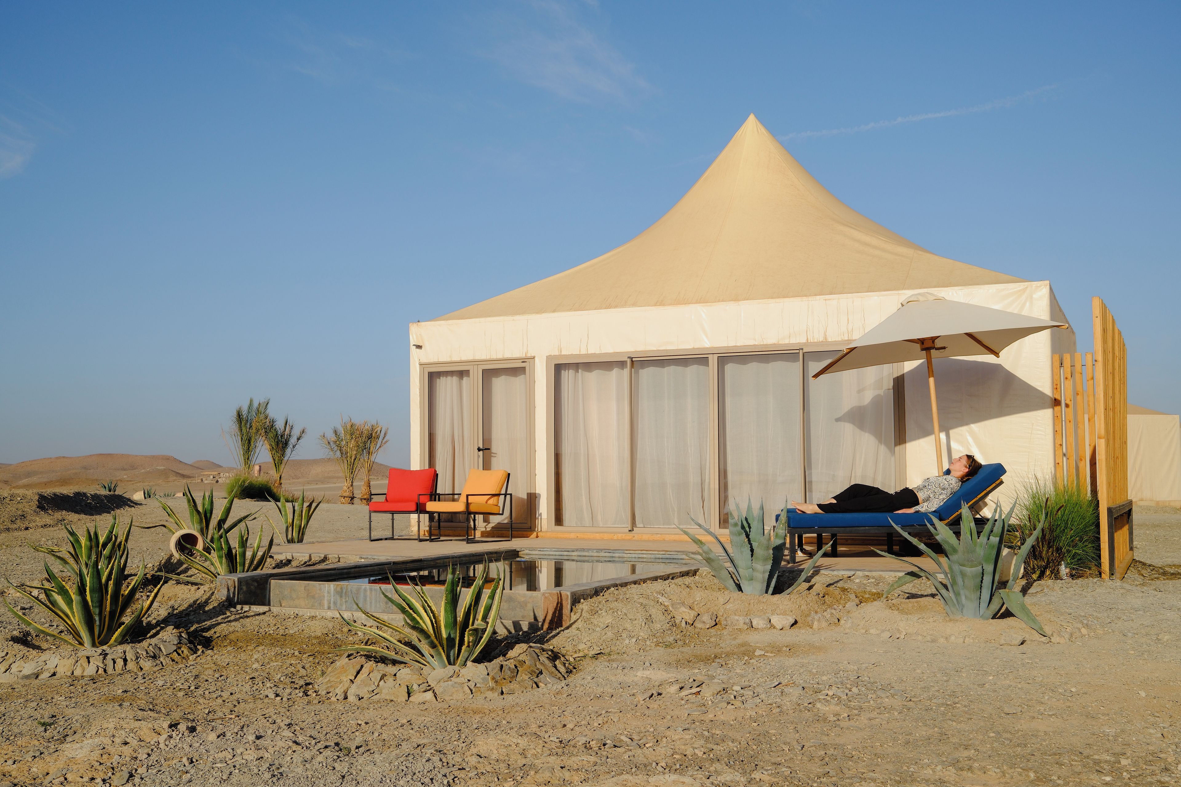 Una tienda de campaña en el desierto con piscina, dos sillones de descanso y plantas del desierto.