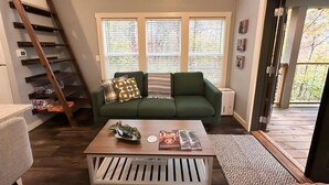 A cozy living room with a green sofa, a wooden coffee table, and a staircase. - 2 Homes Mentone Getaway | Riverfront & Near Parks (Mentone)