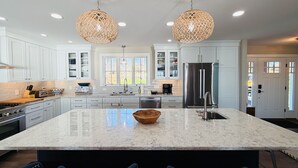 A spacious kitchen with white cabinetry, a large marble island, and two hanging wicker chandeliers. - A Luxury Lakeside Getaway (Aurora)