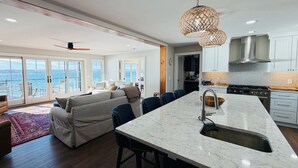 A modern kitchen with a large island, a dining area with a sofa, and a view of the sea through large windows. - A Luxury Lakeside Getaway (Aurora)