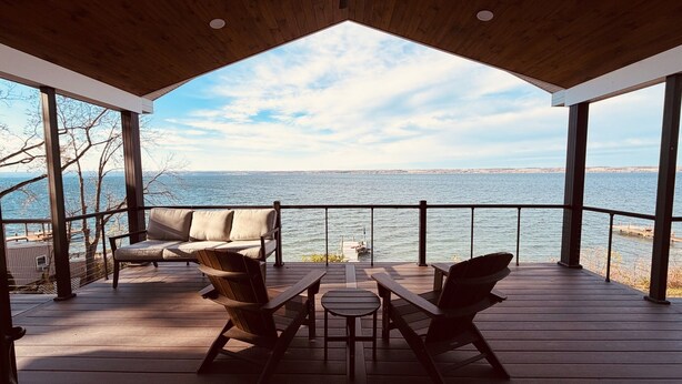 A covered deck with a view of the sea, featuring a sofa, two chairs, and a small table. - A Luxury Lakeside Getaway (Aurora)