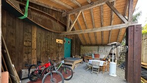 A rustic wooden barn with a gravel floor, two bicycles, a table, chairs, and a stone wall. - Authentic stay in Haut-Doubs (Morteau)