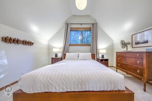 A bedroom with a large bed, two bedside tables, a dresser, a window with curtains, and a wall-mounted light fixture. - NEW Pet-Friendly Original Ski Cabin in Panorama (Panorama)