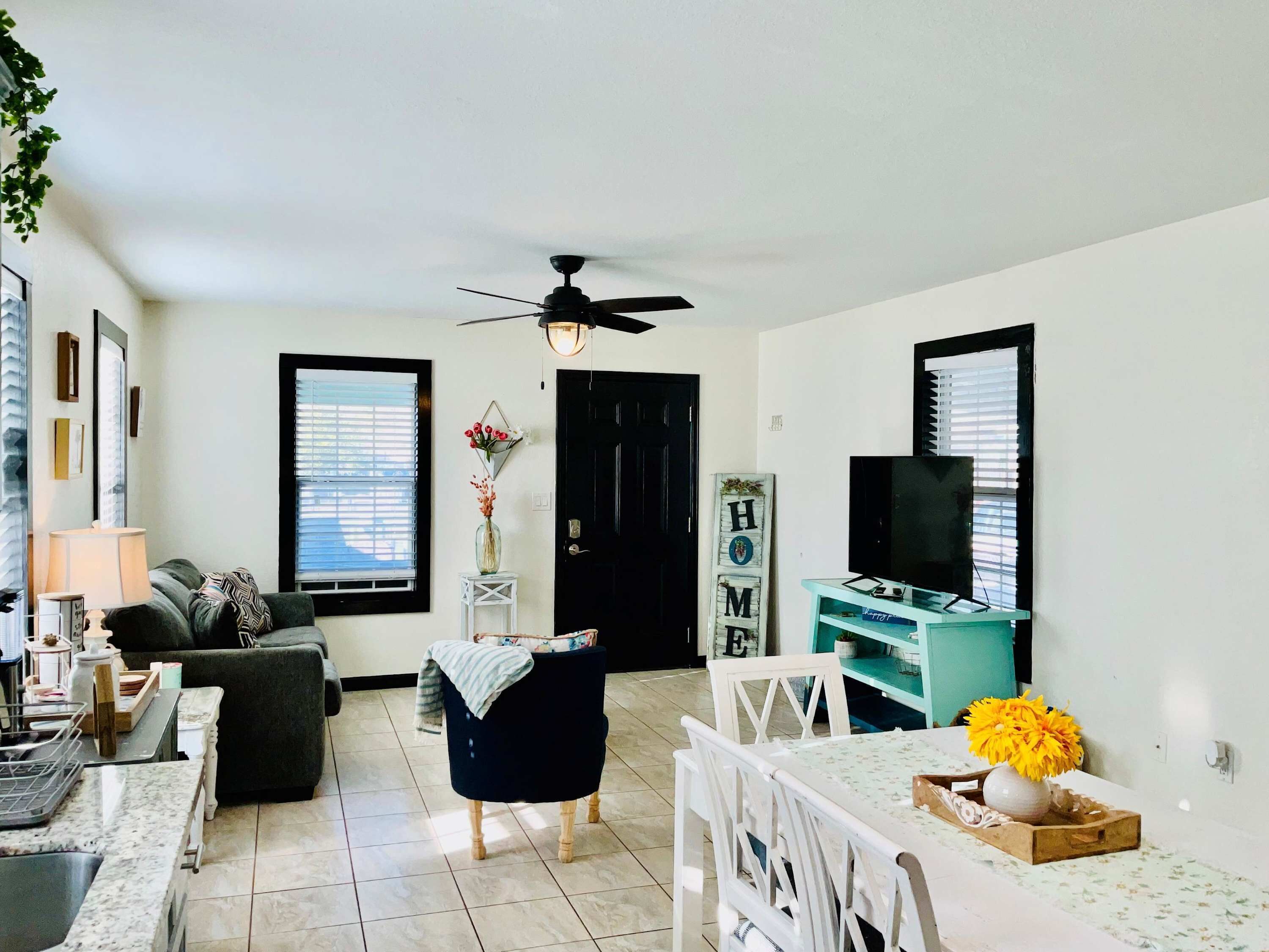 Una sala de estar con sofá, mesa de comedor, sillas, mueble para televisión y ventilador de techo.