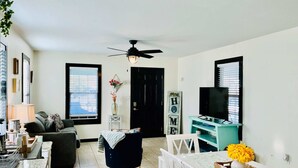 A living room with a sofa, a dining table with chairs, a TV stand, and a ceiling fan. - Urban Aquarium,Home for 8 (Galveston)