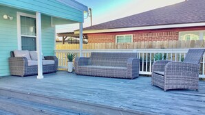 A covered outdoor deck with wicker furniture, a blue building, and a wooden fence. - Urban Aquarium,Home for 8 (Galveston)
