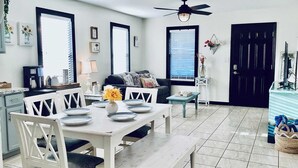A dining area with a white table set for four, a ceiling fan, and a black door in the background. - Urban Aquarium,Home for 8 (Galveston)