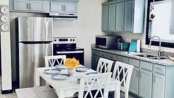 Una cocina con armarios blancos, un refrigerador de acero inoxidable, un microondas y una mesa de comedor con platos y un florero.