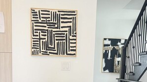 A dining area with a long table set for six, a modern abstract painting above, and a staircase in the background. - Bentley Commons Luxury 3 Bedroom Townhome in the Fallsview Tourist District (Niagara Falls)