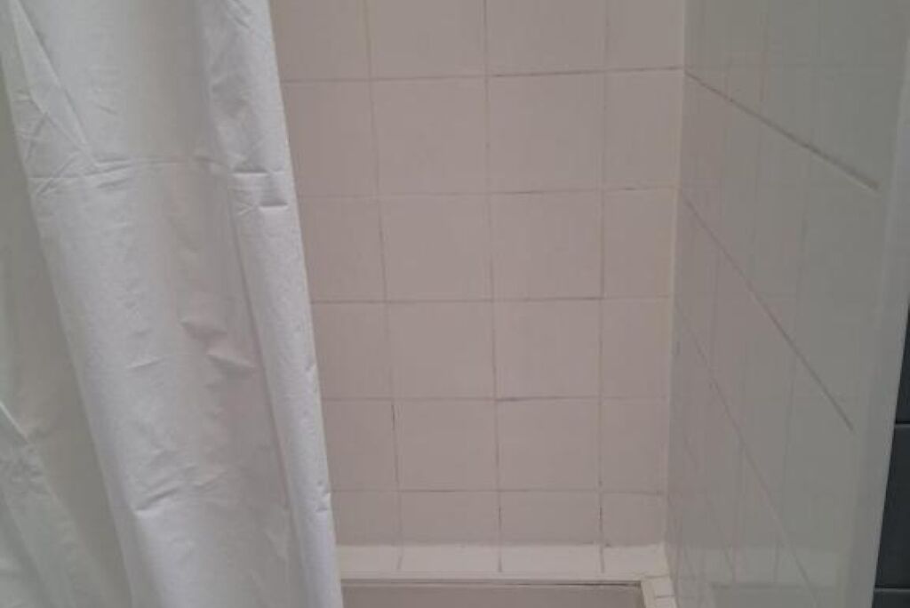 Un baño con paredes de azulejos blancos y una cortina de ducha blanca.