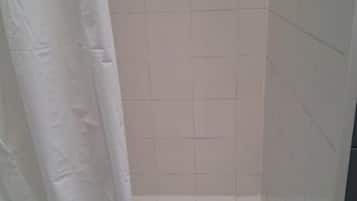 Un baño con paredes de azulejos blancos y una cortina de ducha blanca.