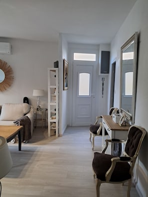 Une pièce comprenant un canapé, une petite table, une lampe, une bibliothèque, un miroir et une porte avec une fenêtre.