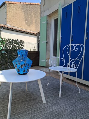Ein runder Tisch mit einer blauen Vase und einem weißen Metallstuhl vor einem Gebäude mit blauen Schließfächern.